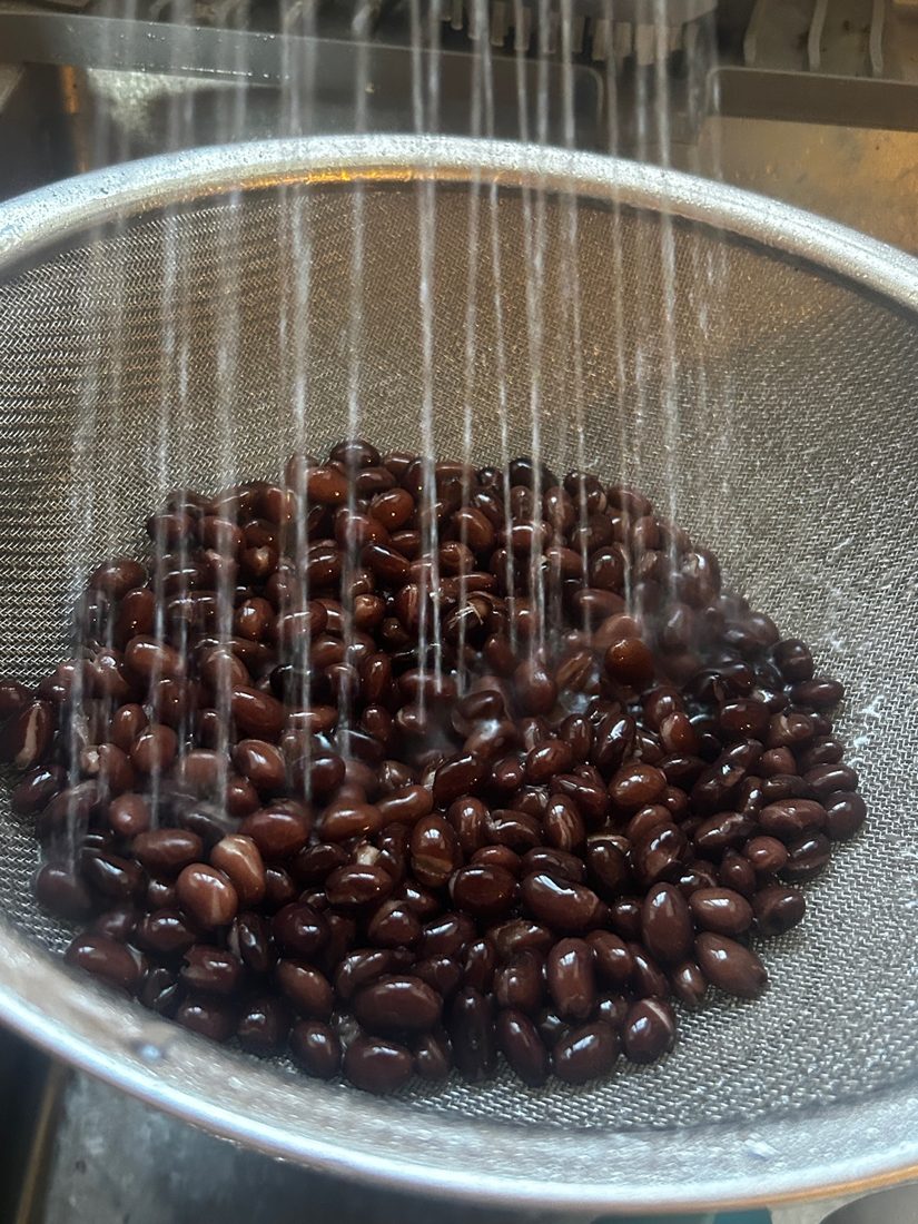 Black beans being rinsed in a strainer under running water