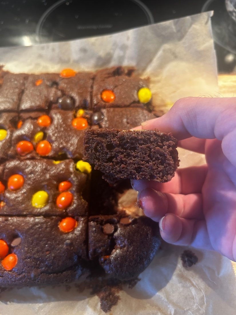 A hand holding a cut brownie showing the dense cross-section